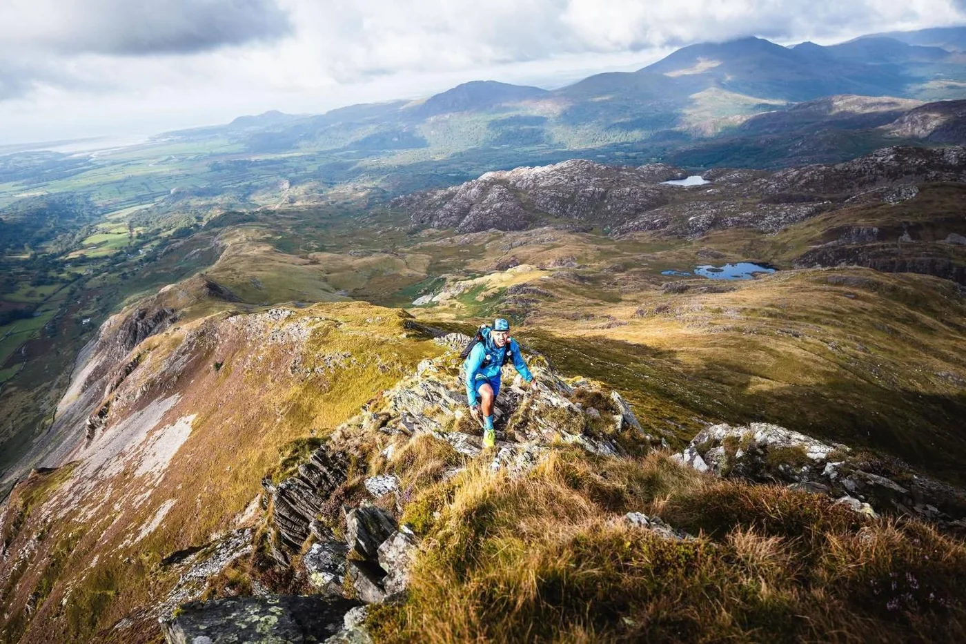 A wide view of a rocky Welsh ridge line with a runner on it and the coast in the distance