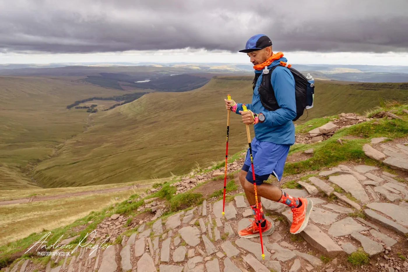 A runner walking a slabbed stone path high on a Welsh mountain, with a valley and reservoir behind