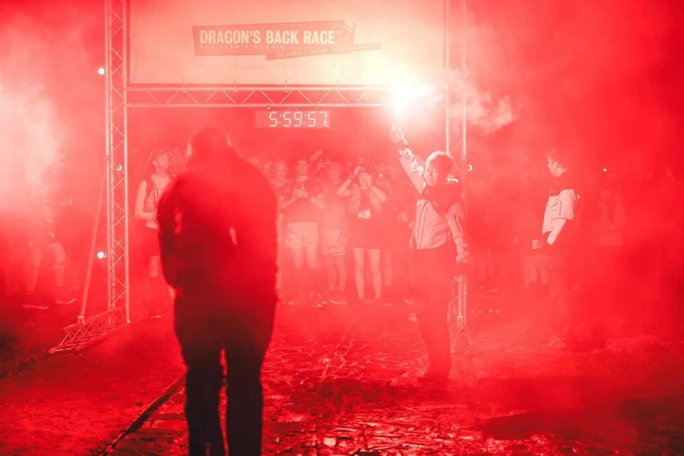 A red flare burning at the Dragon's Back Race start gantry, with the race clock reading 5:59:57