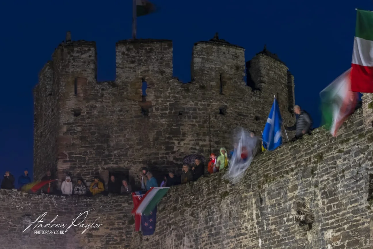 Spectators and national flags on the battlements of Conwy Castle at first light