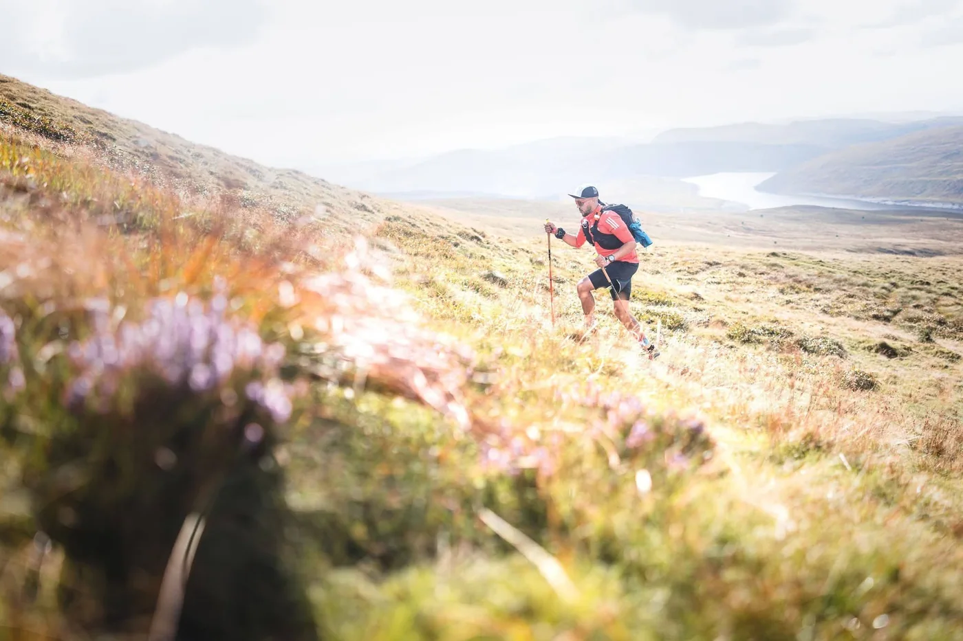 A runner in a red top climbing a grassy mountainside high above a lake in Wales